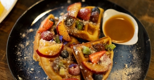 A plate of waffles with fruit and icing sugar, and a pot with caramel sauce