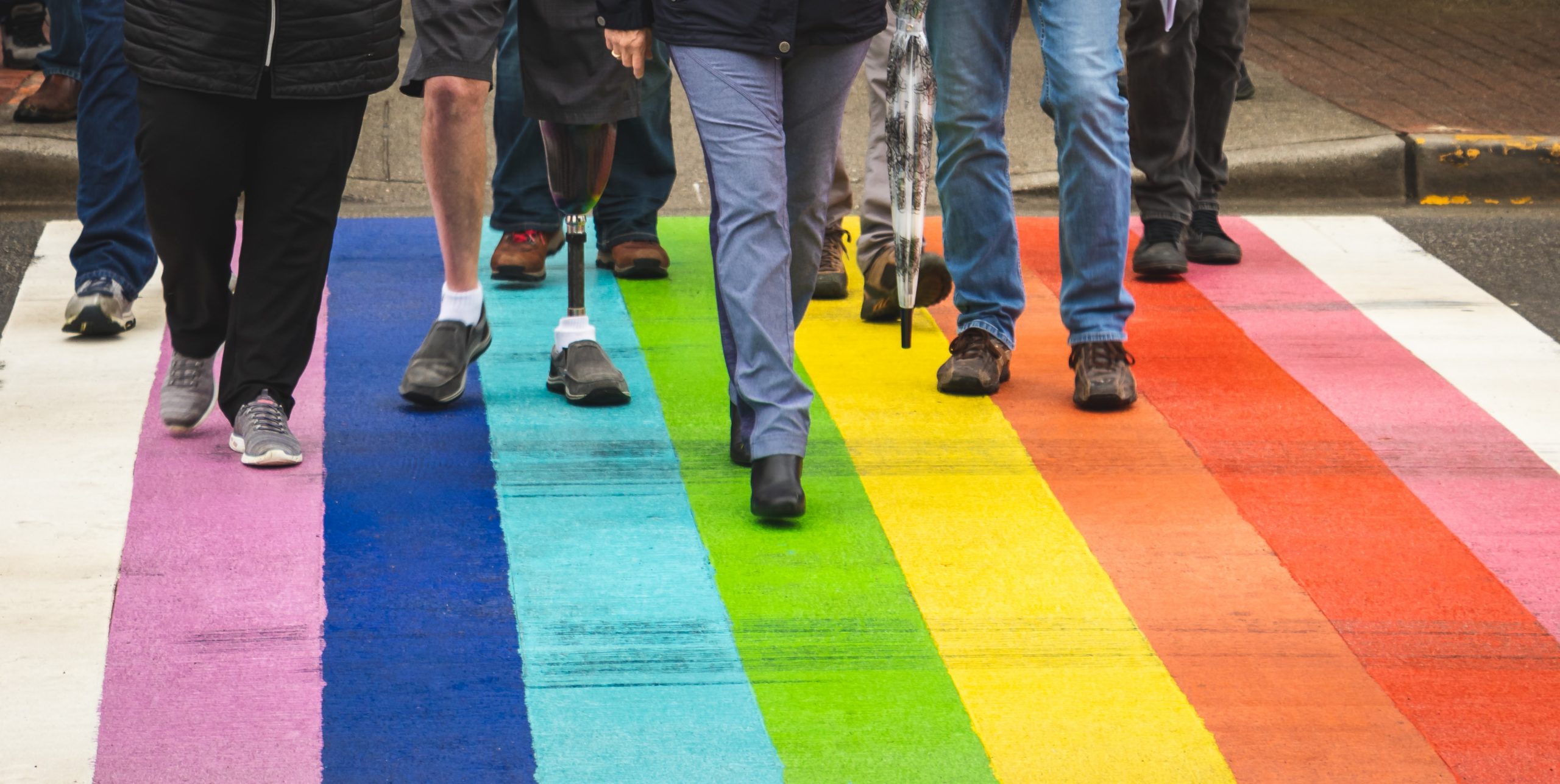 A road with a rainbow painted crossing and a group of people walking across it.