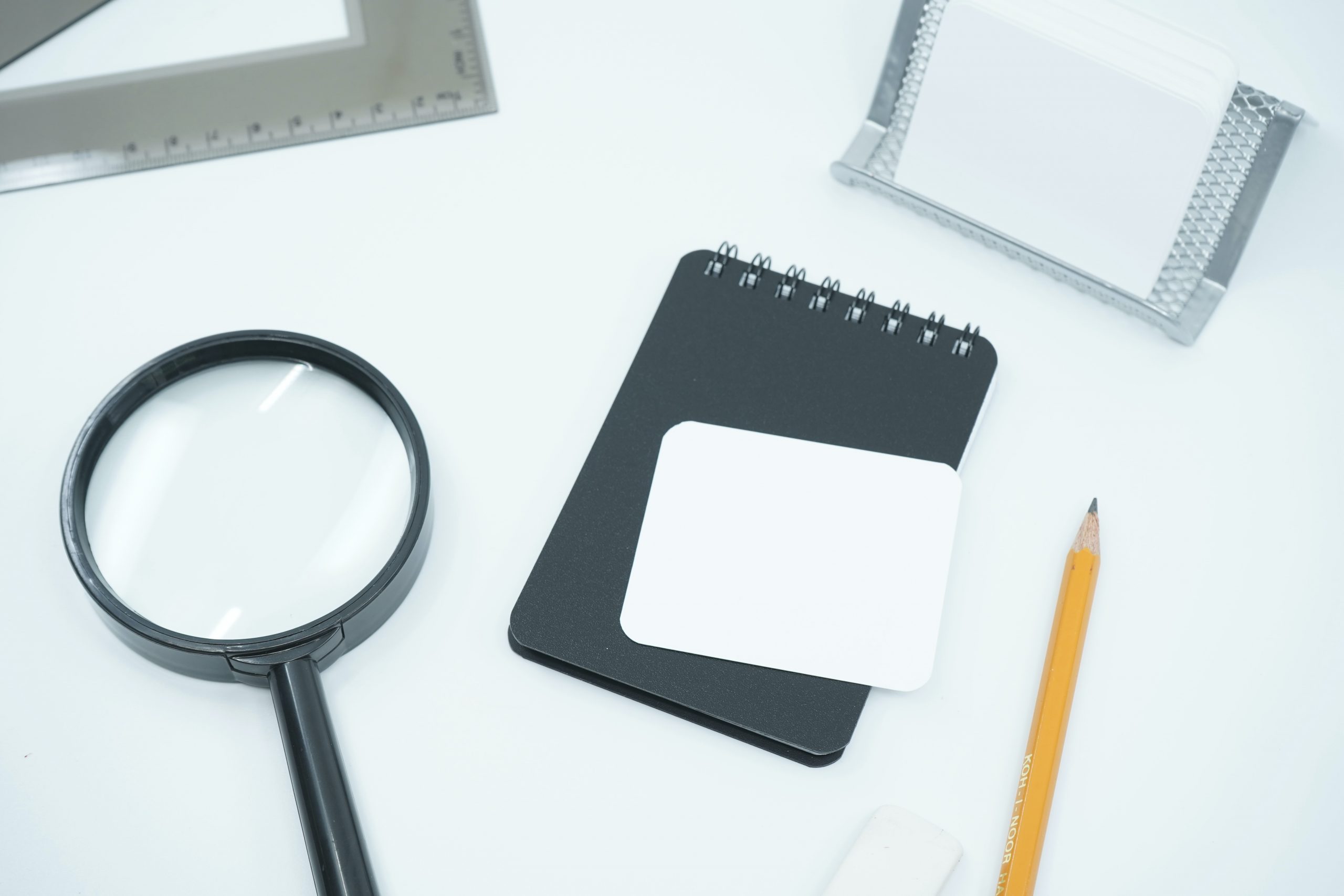 A magnifying glass, a notepad, a pencil and a ruler on a table.