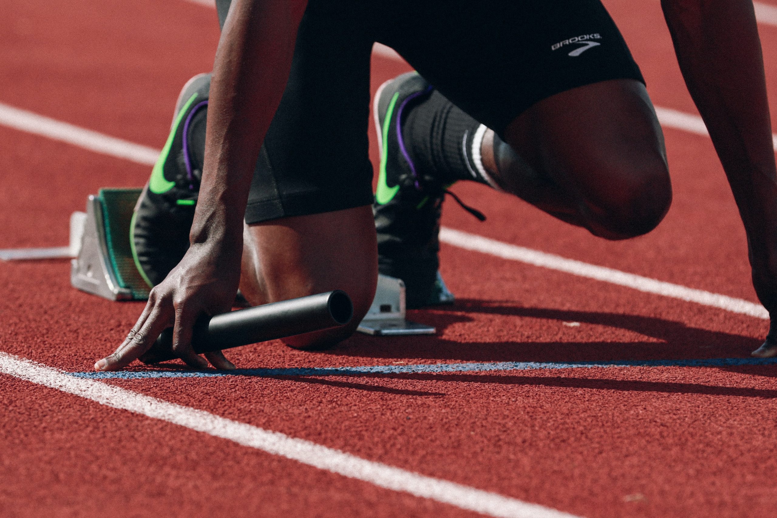 Someone crouching on a racetrack, getting ready to sprint.