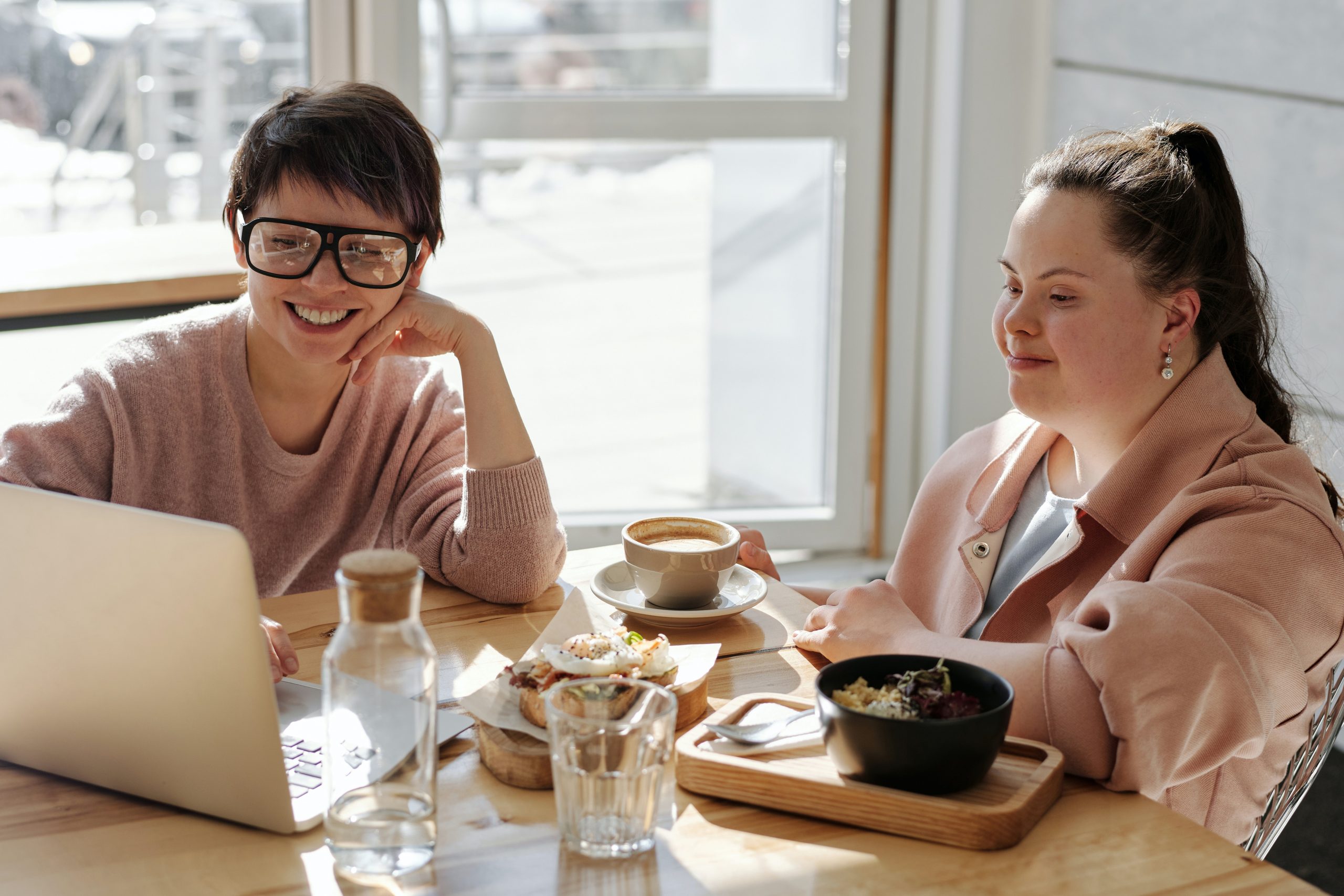 A woman using a laptop sat next to another woman with Down syndrome, both working together.