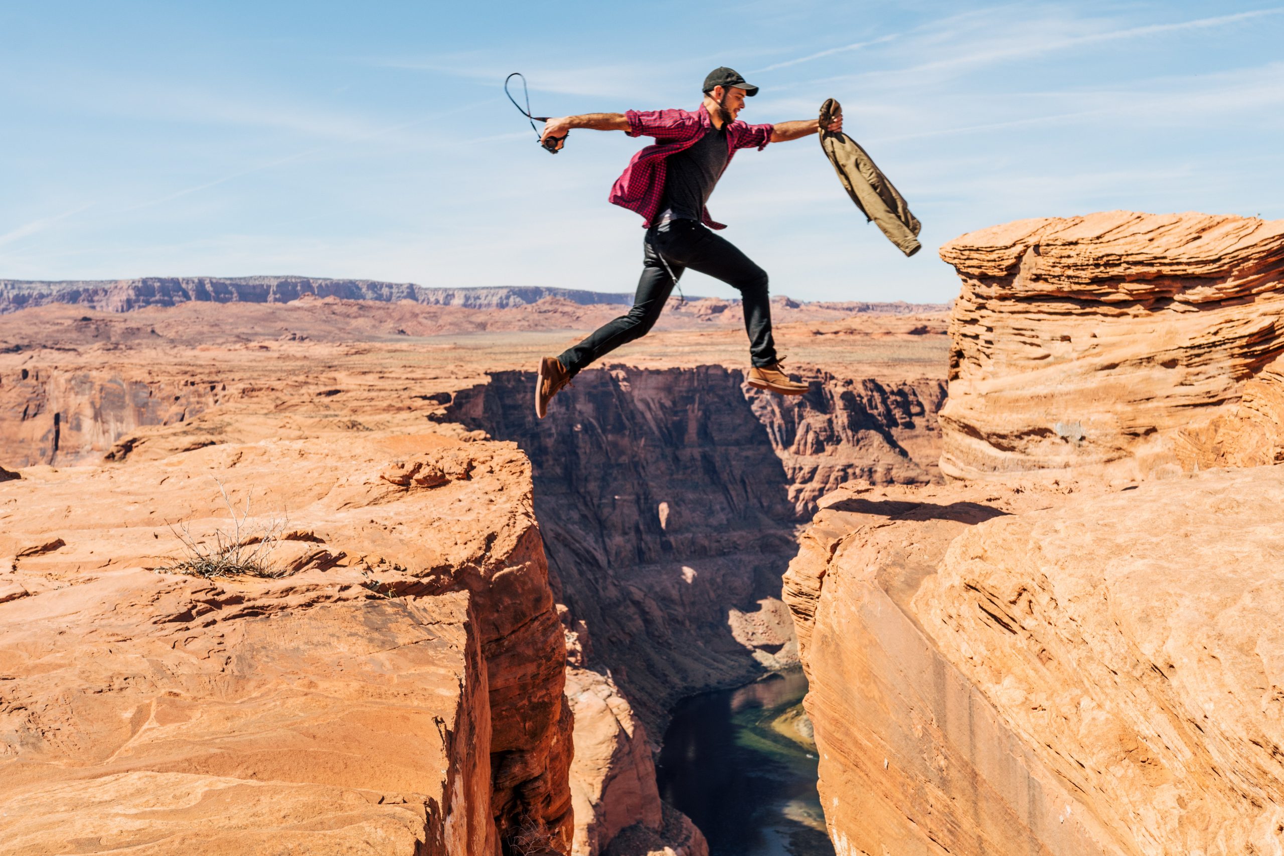 A man leaping over a gap in a sandy gorge.