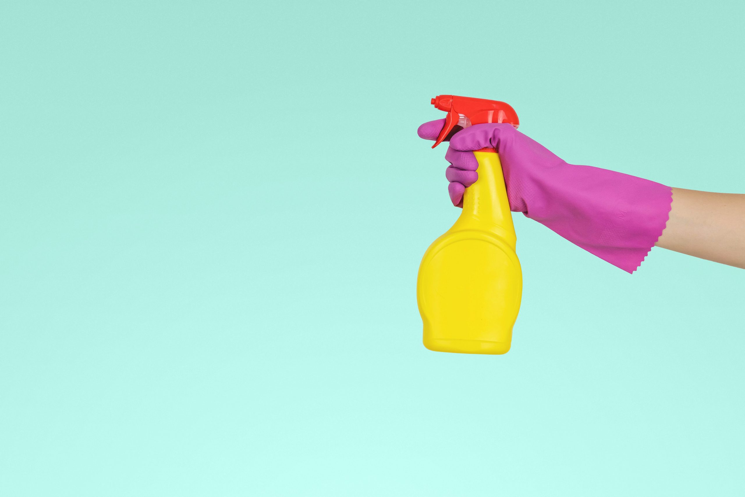 A hand wearing a rubber glove holding some cleaning spray.