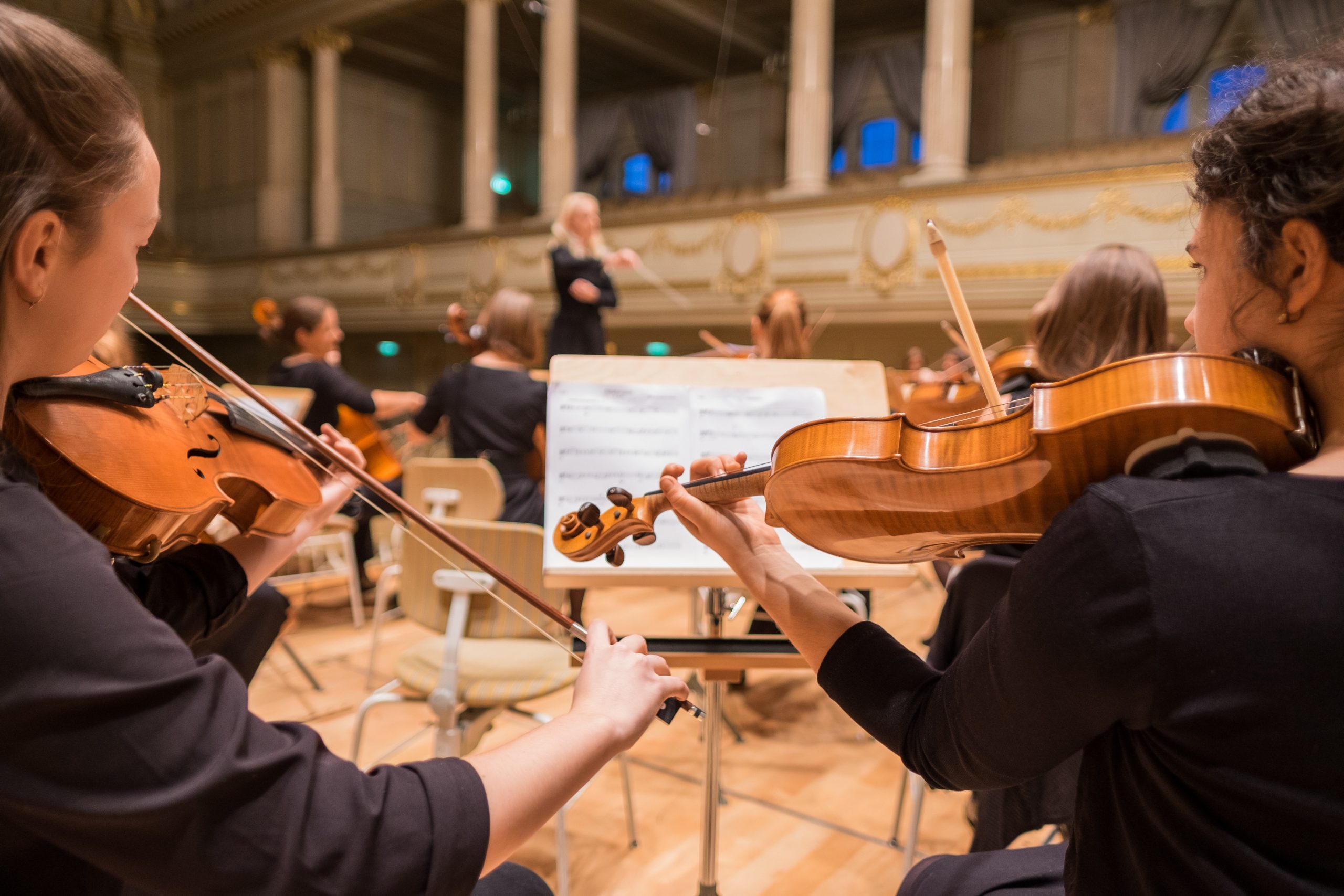 Two violin players rehearsing in a concert hall.